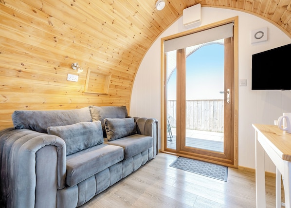 A cozy room with a wooden ceiling, a gray sofa, a wooden table, and a sliding glass door leading to an outdoor deck. - 0 bedroom accommodation in Great Busby (Great Busby)