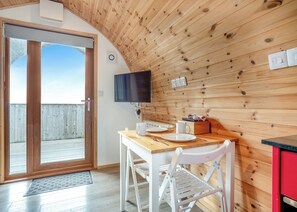 A wooden interior with a dining table, chairs, a television, and a view through a glass door.