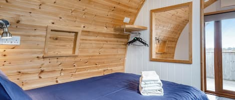 Una habitación con techo de madera, una cama con colchón azul, un espejo y una ventana.