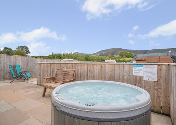 A hot tub with a wooden deck, two lounge chairs, and a wooden fence.