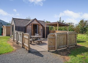 A wooden cabin with a covered patio, picnic table, and a small entrance.