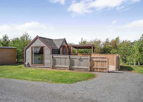 A small wooden cabin with a large window, a covered porch, and a fenced area.