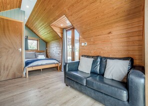 A cozy room with a wooden ceiling, a bed, a leather sofa, and a window.