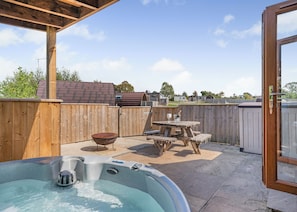 A backyard with a hot tub, wooden deck, picnic table, and a wooden fence.