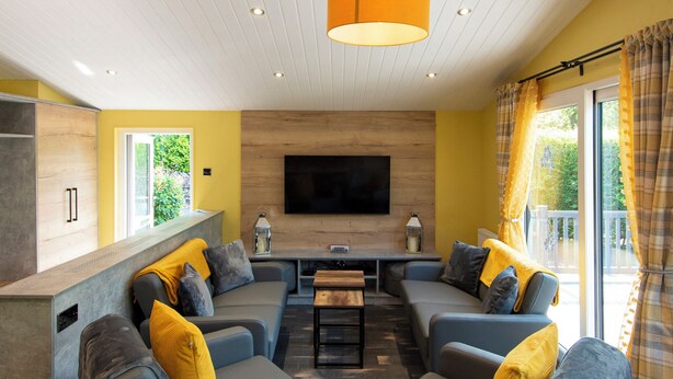 Un salon moderne avec un canapé d’angle, un téléviseur à écran plat et un mur décoratif en bois.
