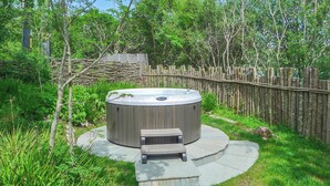 A hot tub with a wooden bench in a garden with a wooden fence and trees.