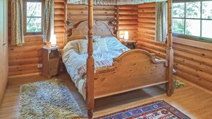 A wooden four-poster bed in a cabin-style room with a window, a nightstand, and a rug.
