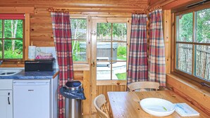 A cabin interior with a kitchen, dining table, and a view of the outdoors.