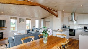 Une cuisine spacieuse avec des poutres en bois, un coin repas avec une table en bois et un salon doté d’un canapé et d’un téléviseur.