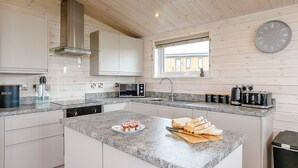 Une cuisine moderne avec des meubles blancs, un plan de travail en granit, un four à micro-ondes encastré, un évier et une horloge murale.