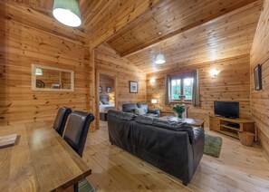 A wooden cabin interior with a dining table, leather sofa, and a television. - 2 bedroom accommodation in Ellesmere (Ellesmere)