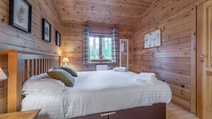 A wooden-paneled room with a bed, a window with curtains, and framed artwork on the walls.