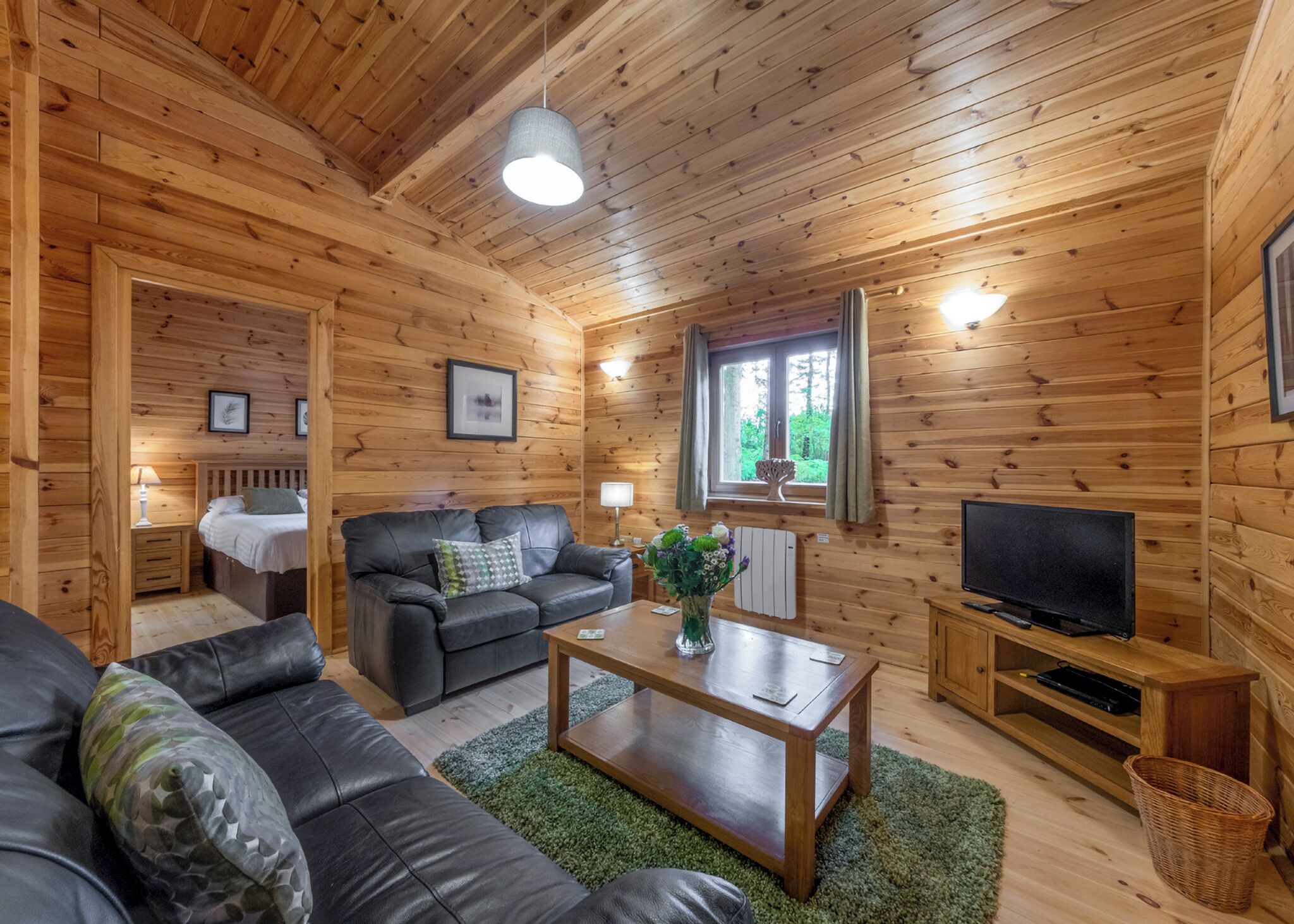 Ein Holzblockhaus-Innenraum mit einer Couch, einem Couchtisch, einem Fernseher und einem Fenster mit Vorhängen.