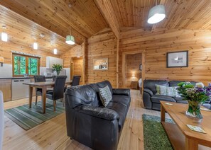 A wooden cabin interior with a dining area, a sofa, a coffee table, and a kitchen.