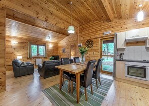 Ein Holzblockhaus-Interieur mit Essbereich, Sofas, einer Küche und einem großen Fenster.