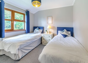 A bedroom with two beds, a nightstand, a lamp, and a window with curtains.