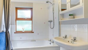 Une salle de bain équipée d’une baignoire, d’une douche, d’un lavabo, d’une fenêtre à vitre dépolie et d’un porte-serviettes.