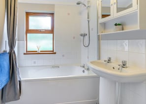 A bathroom with a bathtub, a shower, a sink, a window with frosted glass, and a towel rack.