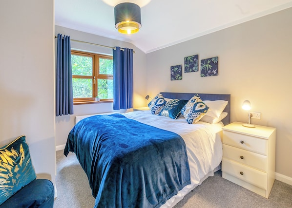 A bedroom with a bed, nightstand, lamp, window with curtains, and wall art.