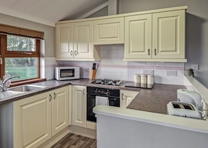 A kitchen with white cabinets, a microwave, a gas stove, a dishwasher, and a window with a view of greenery.