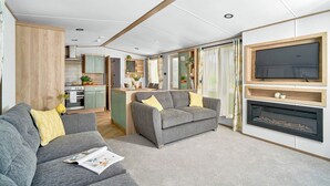 A modern living room with a sofa, a fireplace, and a television mounted on the wall. - Diamond 2 Bed Caravan Hot Tub (Clarach Bay, Nr Aberystwyth)