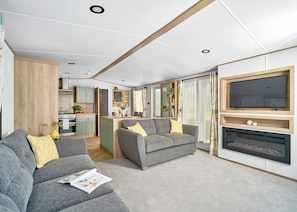 A modern living room with a sofa, a fireplace, and a television mounted on the wall. - Diamond 2 Bed Caravan Hot Tub (Clarach Bay, Nr Aberystwyth)