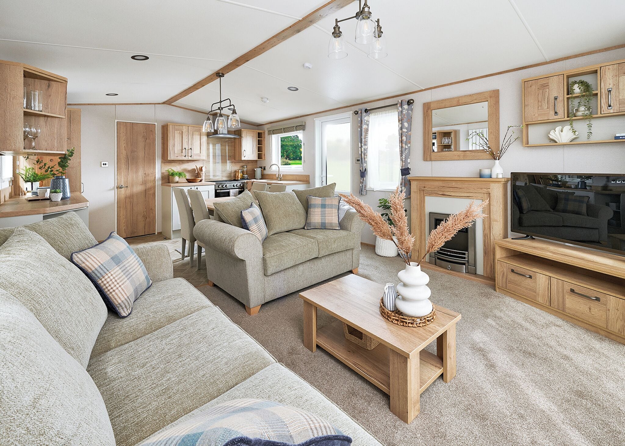 Ein gemütliches Wohnzimmer mit einer Couch, einem Couchtisch und einem Fernseher. Es gibt eine Küchenzeile mit Holzausbau und einem Esstisch.