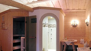 Un interno in legno con zona doccia, panche in legno e un tavolo con una bottiglia.