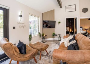 A modern living room with a sofa, two armchairs, a TV, and a wooden slat wall.