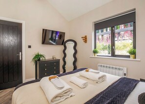 A bedroom with a bed, a dresser, a television, a window with plants, and a radiator. - 2 bedroom accommodation in South Duffield, Nr York (South Duffield, Nr York)
