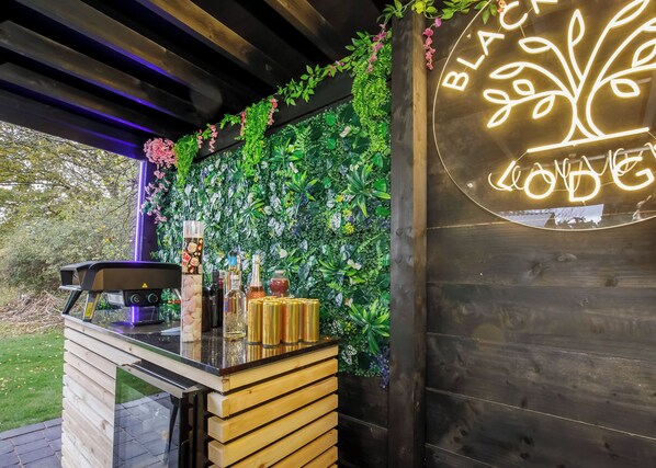 A bar area with a neon sign, wooden counter, and lush green foliage.