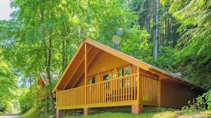 A wooden cabin with a balcony, surrounded by dense forest.