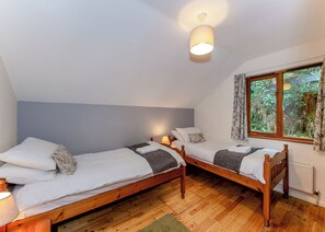 A bedroom with two wooden beds, a window with a view of greenery, a ceiling light, and a radiator.