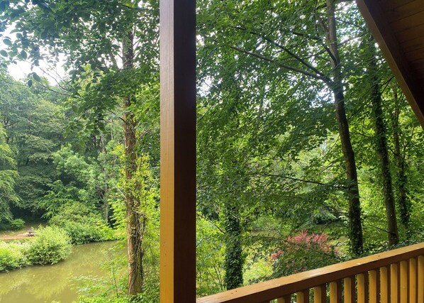 A view of a lush forest with a river, a wooden railing, and a clear sky. - Timber lodge set by the lake with one double and one twin. (Webbery, Bideford)