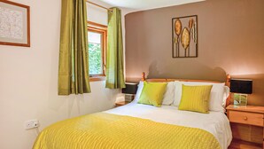 A neatly made bed with a yellow bedspread, green curtains, and a framed botanical artwork on the wall. - 2 bedroom accommodation in Waterrow, Wiveliscombe (Waterrow, Wiveliscombe)