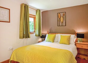 A neatly made bed with a yellow bedspread, green curtains, and a framed botanical artwork on the wall.