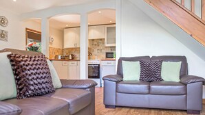 A modern living room with two leather sofas, a staircase, and a kitchen in the background. - 2 bedroom accommodation in Waterrow, Wiveliscombe (Waterrow, Wiveliscombe)