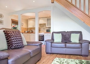 A modern living room with two leather sofas, a staircase, and a kitchen in the background.