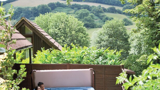 A hot tub in a garden with a view of a house and hills. - 2 bedroom accommodation in Waterrow, Wiveliscombe (Waterrow, Wiveliscombe)