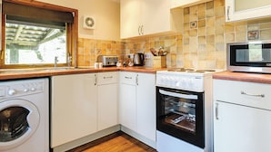 A compact kitchen with a washing machine, oven, microwave, and a window with a view. - 2 bedroom accommodation in Waterrow, Wiveliscombe (Waterrow, Wiveliscombe)