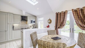 Une cuisine avec des meubles blancs, un îlot central et un coin repas comprenant des chaises en osier et une table ronde.