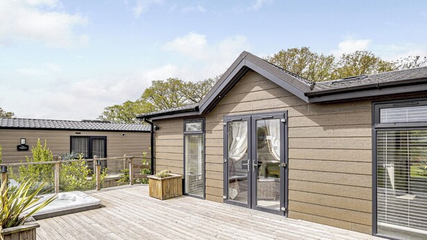 Un bâtiment moderne doté d’une terrasse en bois, d’une porte-fenêtre coulissante et d’un petit espace extérieur aménagé pour s’asseoir.