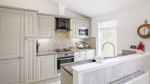 Une cuisine moderne avec des meubles blancs, une cuisinière à gaz, un four à micro-ondes et une fenêtre équipée de stores.