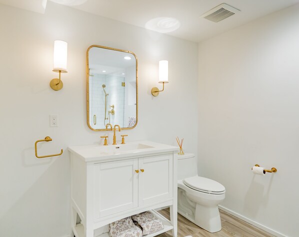 A modern bathroom with a white vanity, gold fixtures, and a large mirror.