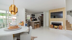 Una cocina moderna con una isla central, una zona de comedor con una mesa redonda y un salón con chimenea.
