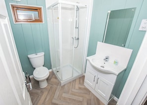 A bathroom with a toilet, a glass-enclosed shower, and a sink with cabinets.