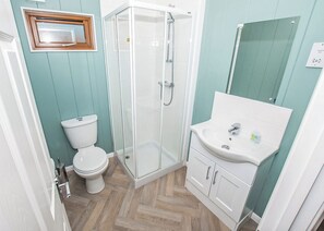 A bathroom with a toilet, a glass-enclosed shower, and a sink with cabinets.