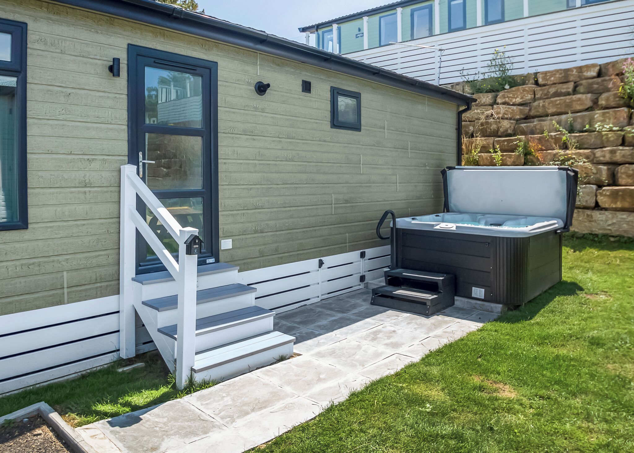 A modern outdoor hot tub area with a stone wall and a wooden deck.