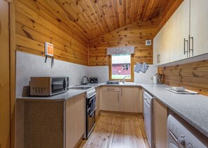 Eine kompakte Küche mit Holzboden, einer Mikrowelle, einem Wasserkocher, einem Spülbecken und einem Fenster mit Blick auf ein rotes Gebäude.