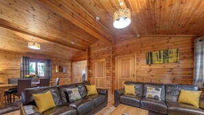 A log cabin interior with two leather sofas, a wooden coffee table, and a dining area with a table and chairs. - Woodland Birch Lodge (Ellesmere)
